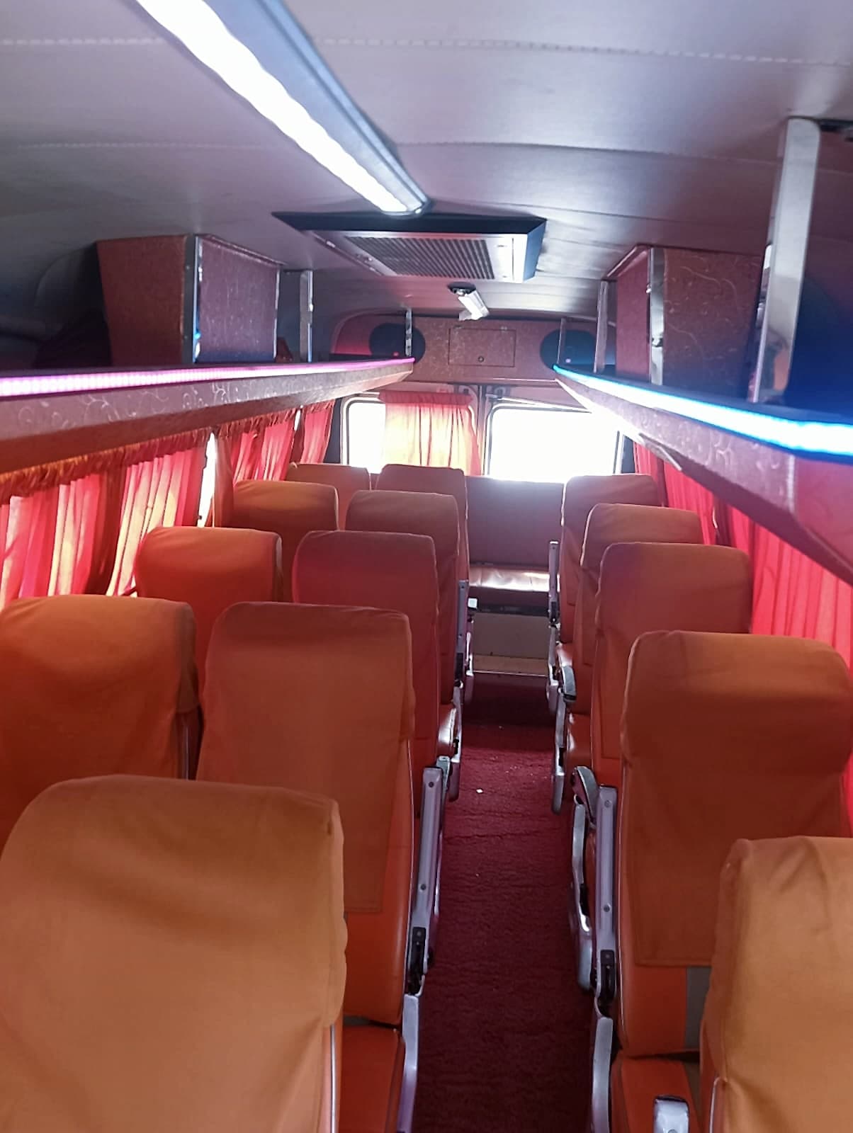 Rows of orange seats with red curtains inside the Kalika Traveller